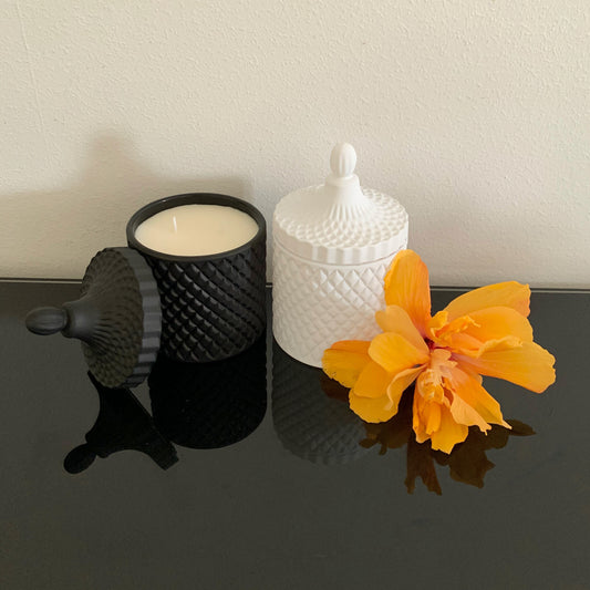 Two Large Geo Candles, Matte Black and Matte White colours, atop a black table with an orange flower.